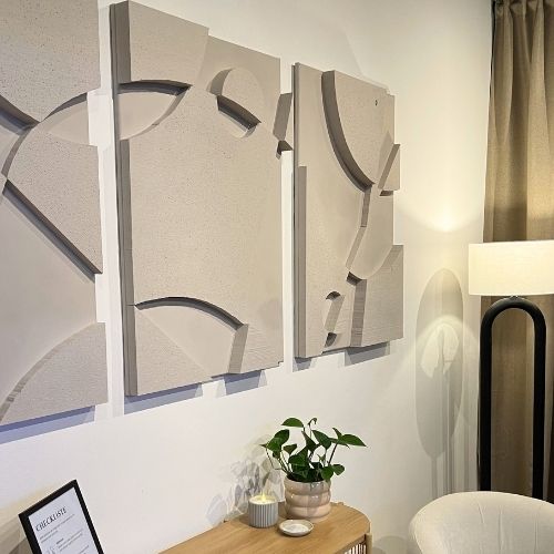 The lounge in the cryo studio of testimonial Eva S. The three pieces of abstract 3D wall art which make up the Warrior Series are hung above a wooden side board with a plant and a lamp.