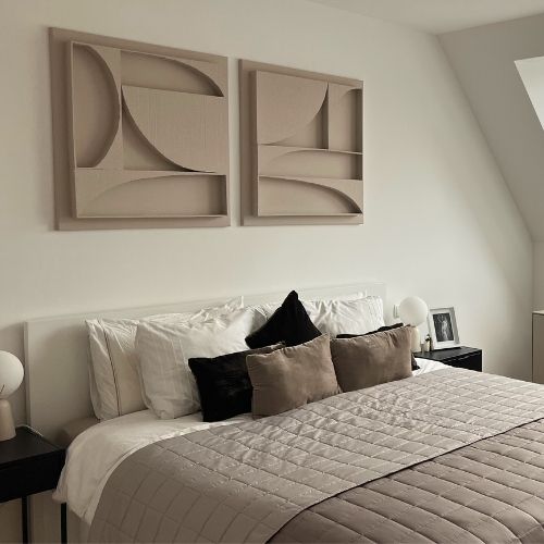 The bedroom of testimonial Alexander R. The two pieces of 3D structural wall art which make up the Karma Series are hung above a beautifully styled master bed, complete with bedspread, decorative pillows and night lights, all held in beige, brown and white tones.